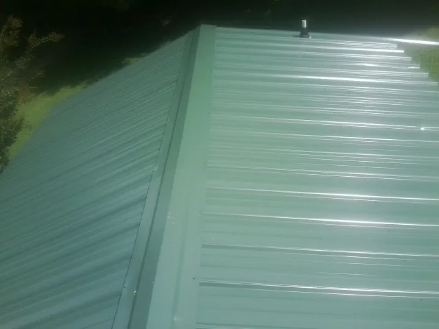 New green metal panels meeting at the ridge of a roof — Flat Roof Repair work by our crew in Perrysburg
